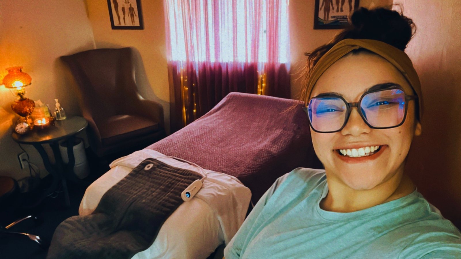 Valerie in her treatment room, with a warm lamp, anatomy charts, and a heated massage table